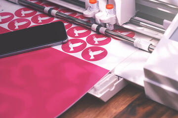 plotting machine on warm brown wooden table cuts pink peace dove stickers from adhesive foil in...
