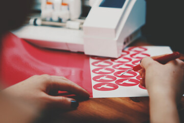 women hands with painted nails use tool to weed freshly cut pink peace dove stickers. wooden...