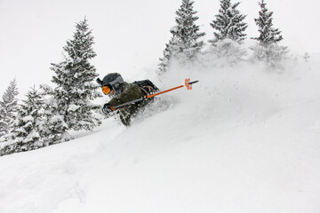 Side view of a man sliding down the snowy mountain slope and splashing snow around him