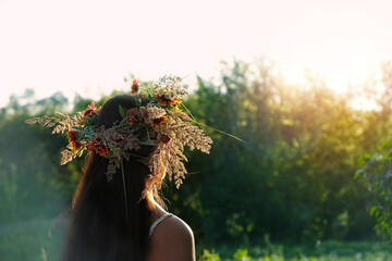Girl in flower wreath on meadow, sunny green natural background. Floral crown, symbol of summer...