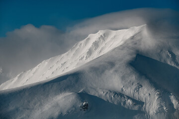 Scenic view on snowy mountain peak covered with clouds in sunny day