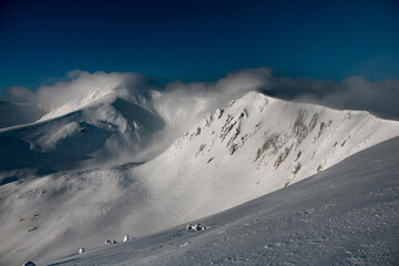 Scenic view on snowy mountain peaks covered with clouds in sunny day