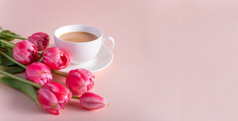 Fototapeta na wymiar Banner.One cup of hot, morning coffee and a bouquet of pink-lilac tulips on a bright pink background. View from above.Copy space for text. The concept of holidays.