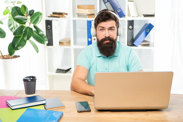 Serious man listening to webinar in headphones using laptop in office, online education