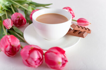 Obraz na płótnie Canvas Banner.One cup of hot morning coffee, milk chocolate and a bouquet of pink-lilac tulips on a bright white background. View from above. Copy space for text. Holidays concept.