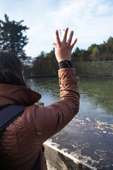 Woman in a Coat Throwing Pebbles in the Lake at the palace of versailles, 
with trees in the background