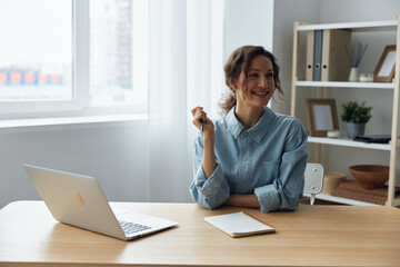 Dreaming thoughtful cheerful smart gorgeous pensive curly businesswoman think about weekend smiling looks aside using laptop in office. Modern Job Remote Work concept