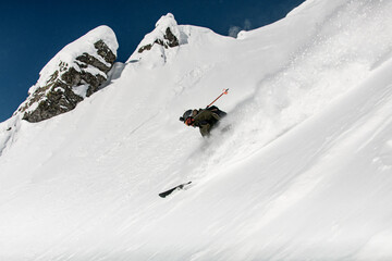 Freerider skier with go-pro camera on his helmet fast sliding down snow covered slope.