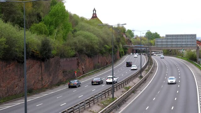 High angle blurred view of M60 motorway highway traffic by red cliff in Stockport town, Greater Manchester, United Kingdom.