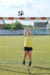 Girl goalie with overweight stands in football gate and jumps to catch the ball with his hands