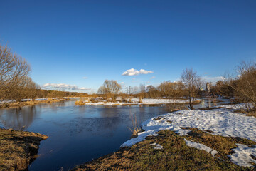 March sunny day by the river. A picturesque landscape, early spring, a river with snow-covered banks. The first thaws, the snow is melting.