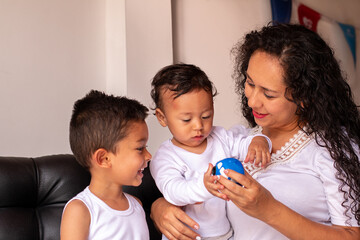 A young baby and toddler playing with their mother with a toy cart. Frizzy haired latin mother teaching her children to play.