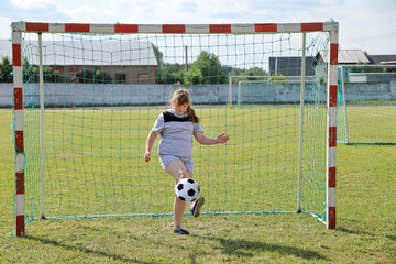 Chubby girl in sportswear stands in football gate and beats the ball with his foot