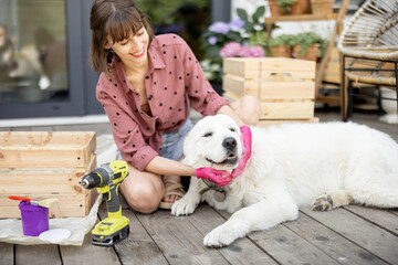 Young cheerful housewife makes wooden boxes while sitting with her dog on wooden terrace of her house. Diy and housework concept. Idea of friendship with pets