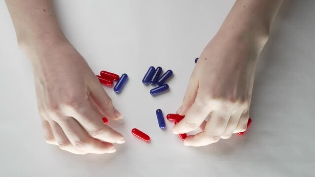 A woman on a white table sorts red and blue pills.