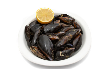 Raw mussels in a white bowl, with half a lemon, isolated on white background. It feeds on phytoplankton and zooplankton, and even decomposing organic particles found in seawater.