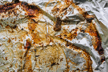 Background, texture, top view of a dirty, greased, sunflower oil, meat dish, colored foil. Photo after cooking.