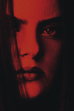 Fashion, style, makeup concept. Beautiful woman with long dark hair close-up studio portrait. Face partly covered with shadow. Red filter with grain applied to make horror and mystique atmosphere
