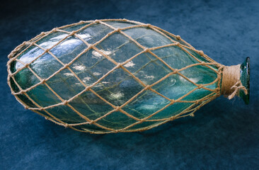 On  blue background is  large glass bottle covered with  woven net of coarse rope.