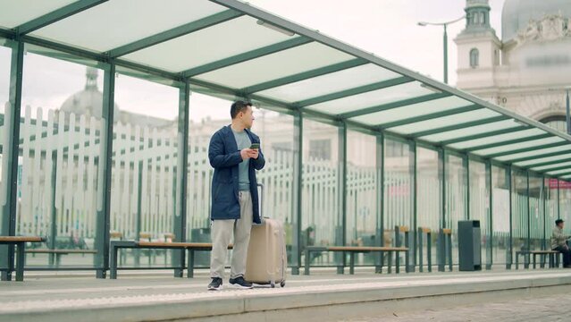 Senior Chinese tourist uses mobile phone app to book accommodation and call taxi, man near airport with suitcase. Asian man using smartphone app to rent a car at the bus stop. waiting public transport