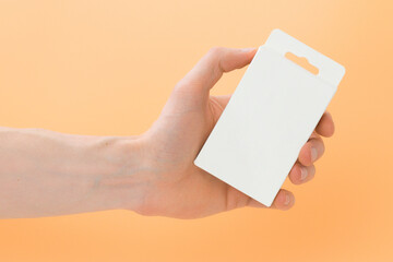 Man's hand holds a white package with a hanging hole on a yellow background. Closed. Rectangular....