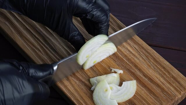 Chef cuts fresh onions with old knife into pices on wooden cutting board. Preparation of ingredients