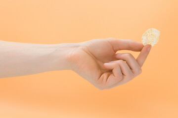 The man's hand turned up and holds a piece of rice chips on yellow background. Dietary. Slice. Ingredient. Circle. Man. Male. Arm