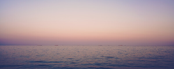 Fototapeta na wymiar Beautiful panoramic view to calm sea surface with cargo tanks on horizon line at sunset