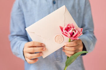 Anonymous child holding pink envelope with gift certificate and tulip in his hands.Mother day concept or present for moms.