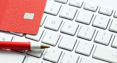 A pen and a credit card placed on a white computer keyboard.