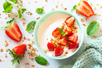 Yogurt with granola and strawberry in blue bowl at light stone table. Top view.