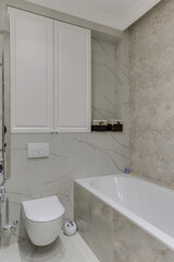 Corner of a bright modern toilet in white tiles with toilet and bath