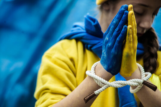 girl with a braid in a yellow sweater on a blue background with tied hands painted in blue and yellow Ukrainian flag