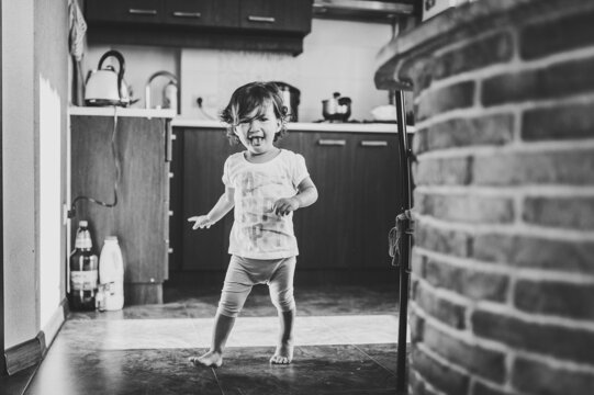 Funny toddler girl dancing indoors, little child play, baby having fun moving and jumping on the floor in a sunny white room at home or kindergarten. Black and white photo.