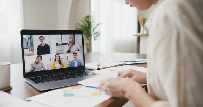 Young asia female listen leader on video call with diverse multiracial colleagues on online with laptop in kitchen at house. Girl student distance learn online at house, Online meeting concept.