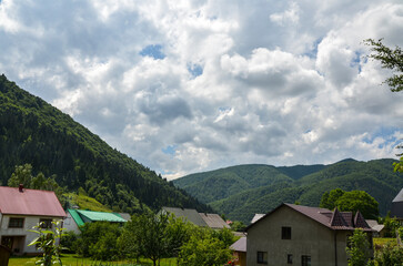 Fototapeta na wymiar Picturesque landscape оf mountain village Kolochava with green grassy meadow, houses and mountains covered forest on a sunny summer day. Carpathians, Ukraine
