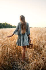 Fototapeta Cottagecore, simple living, slow life, country aesthetic lifestyle, modern rural fantasy, pastoral aesthetic. Young girl in peasant dress with straw handbag enjoying nature on sunset obraz