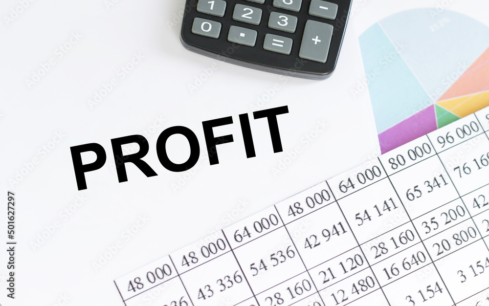 Aufkleber profit text on a notepad on a table next to charts, reports and a calculator