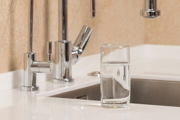 a glass of clean transparent drinking water stands on the kitchen table