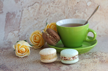 Multi-colored macaroons. Tea drinking. Green cup with hot tea and saucer on an abstract background. Macaroons are a popular dessert