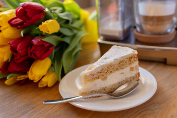 Cup of coffee with milk, piece of cake and tulips flowers on wooden kitchen table. Freshly brewed cappuccino espresso in coffee machine for breakfast. Stylish home interior decor. . High quality photo