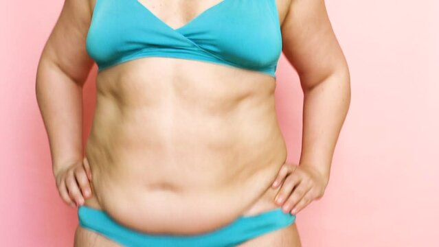 Confident and playful woman with excess weight in blue swimsuit, shaking fat on stomach and sides. Body positive and acceptance, love your body. Wiggling and bouncing shaking stomach. Belly dancing