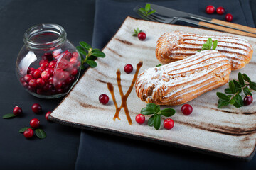 Cream eclairs choux pastries served with fresh cranberries on a handmade ceramic plate. Profiterole cupcakes - 501634026