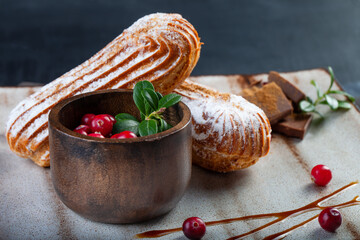 Cream eclairs choux pastries served with fresh cranberries on a handmade ceramic plate. Profiterole cupcakes - 501634027