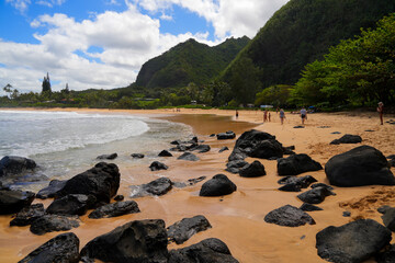 Black rocks stranded on the sand of Cannon's Beach next to Haena Beach Park on the North Shore of Kauai island in Hawaii, United States - obrazy, fototapety, plakaty