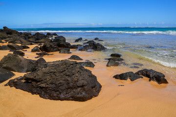 Black rocks stranded on the sand of Cannon's Beach on the North Shore of Kauai island in Hawaii, United States - obrazy, fototapety, plakaty
