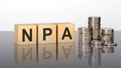 npa - text on wooden cubes on a cold grey light background with stacks coins