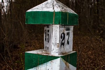 Weathered wooden pole painted in white and green showing the distance of 25 and 27 miles or kilometers. Vintage travel milestone landmark in forest