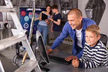 Fototapeta na wymiar Interested young man with his tween son using computer to find solution to puzzle in escape room stylized as abandoned bunker