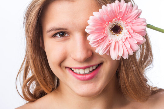 Portrait of a happy girl with fresh skin holding a flower over one eye on white background. Close up portrait of beautiful redhead curly woman pnik flower wearing white tshirt. Beauty and spring